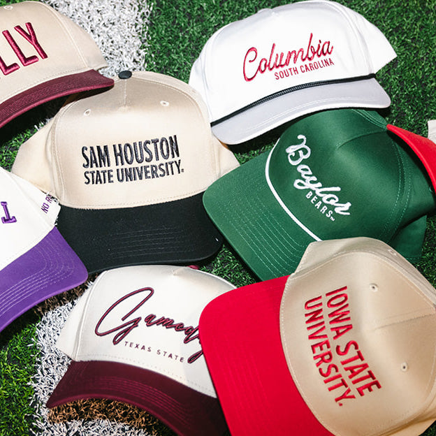 Collection of college-themed caps on a grassy background