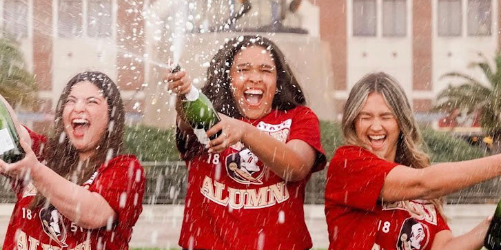 3 girls wearing Florida State alumni tshirts and popping champagne bottles